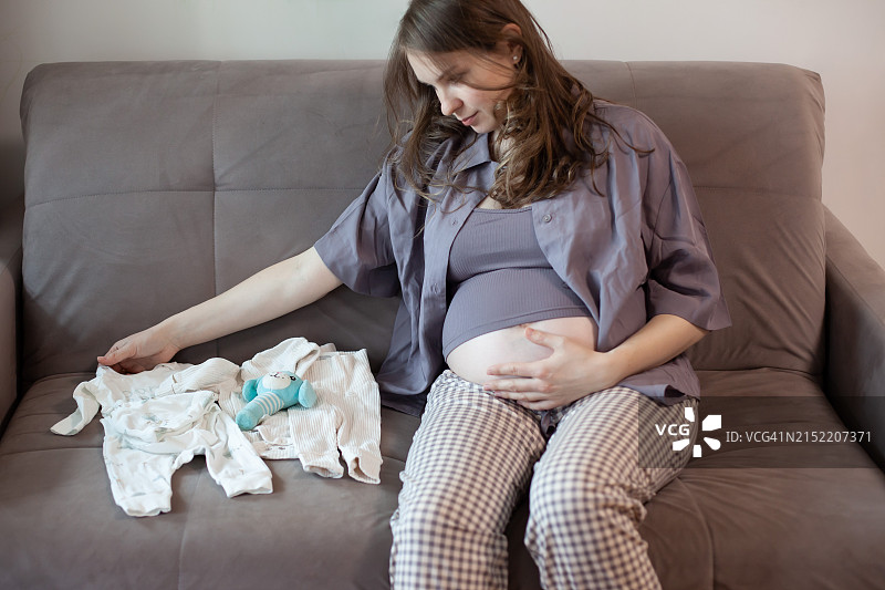 孕妇坐在沙发上看着孩子的东西图片素材
