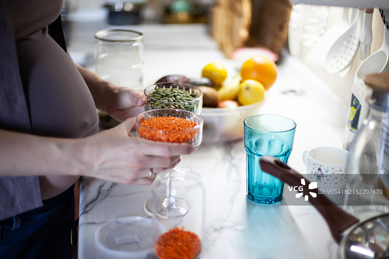 孕妇手中拿着装有红色和绿色扁豆的两个玻璃杯图片素材