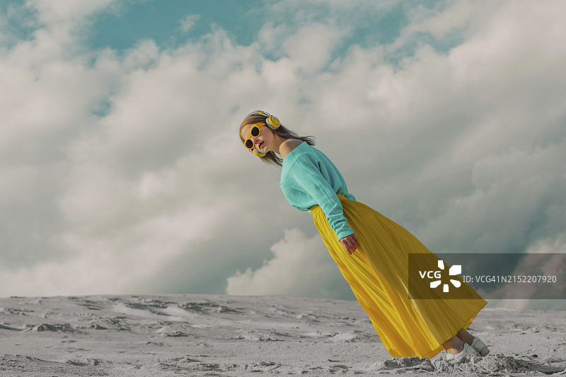 戴太阳镜和无线耳机站在沙丘下的女人图片素材