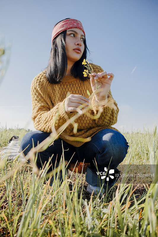 年轻女人拿着花蹲在田野里图片素材
