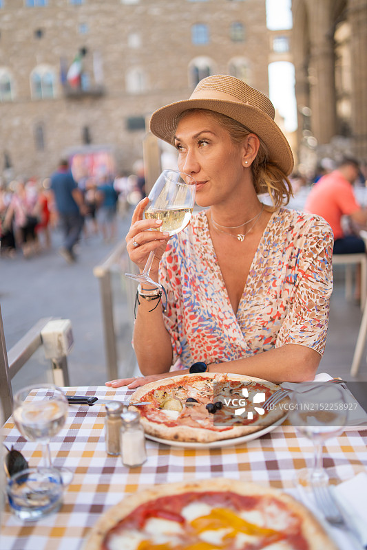 戴帽女子在户外品尝葡萄酒和披萨图片素材