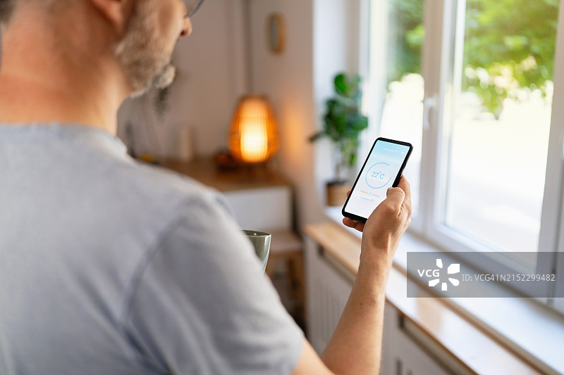 男人拿着手机，运行智能家居温度控制应用程序图片素材