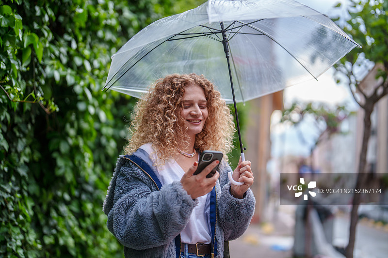 女人在街上撑着伞使用手机图片素材