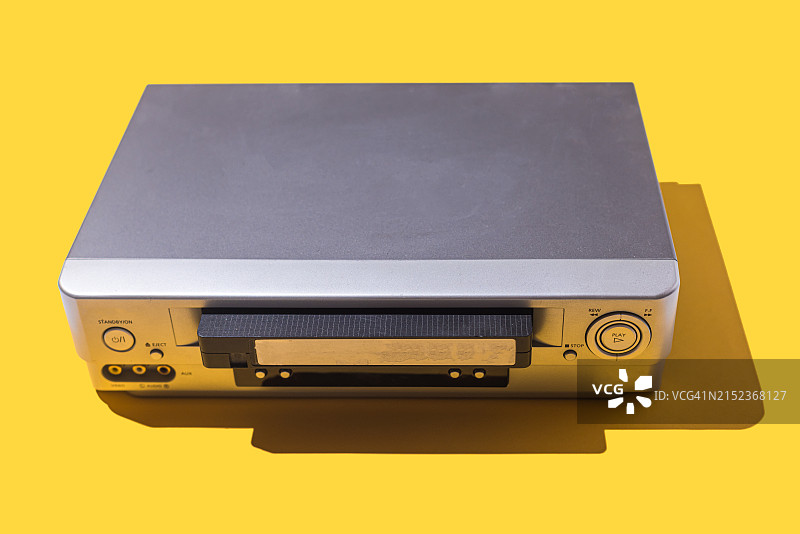 黄色背景上半插入磁带的VHS录像机，复古音像概念图片素材