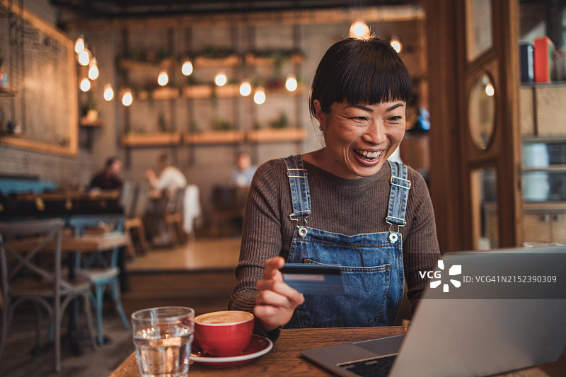 日本女性坐在咖啡馆里，用笔记本电脑在网上购物或通过手机银行查看她的银行账户图片素材