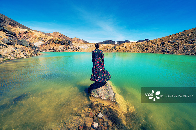 短发女孩身穿连衣裙站在汤加里罗国家公园的绿松石湖泊中的岩石上图片素材