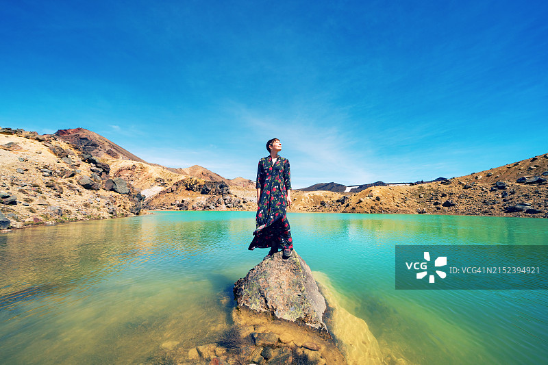 短发女孩身穿连衣裙站在汤加里罗国家公园的绿松石湖泊中的岩石上图片素材