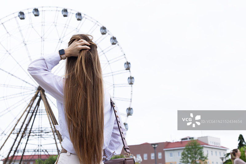 穿着裤子和衬衫站在游乐园里微笑的年轻女子图片素材