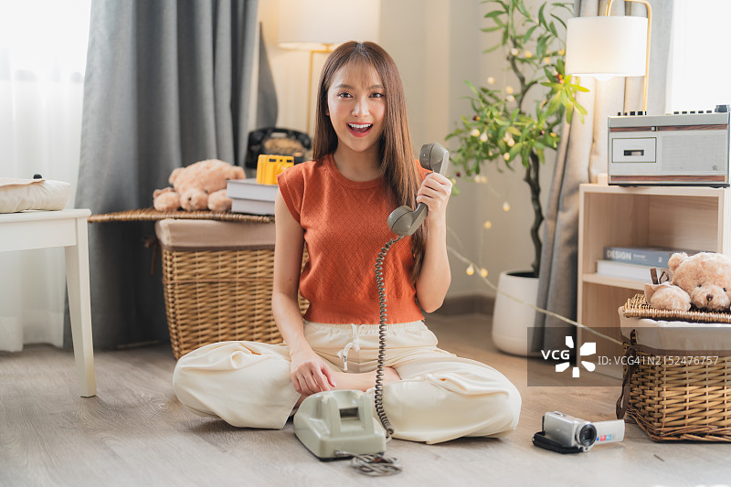 坐在家里木地板上，用老式转盘电话与人交谈的迷人亚洲女子图片素材
