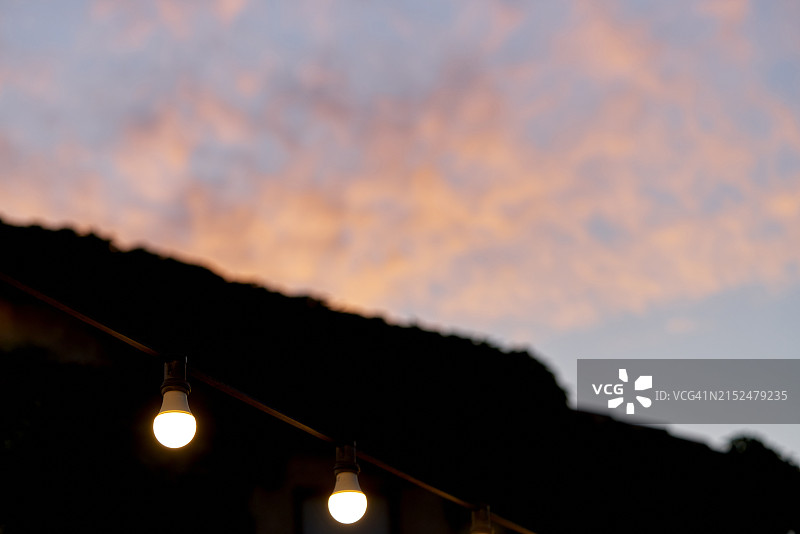 从两层房屋的露台看到的日落和被云层环绕的昏暗天空，被带有不同LED聚光灯的电灯照亮图片素材