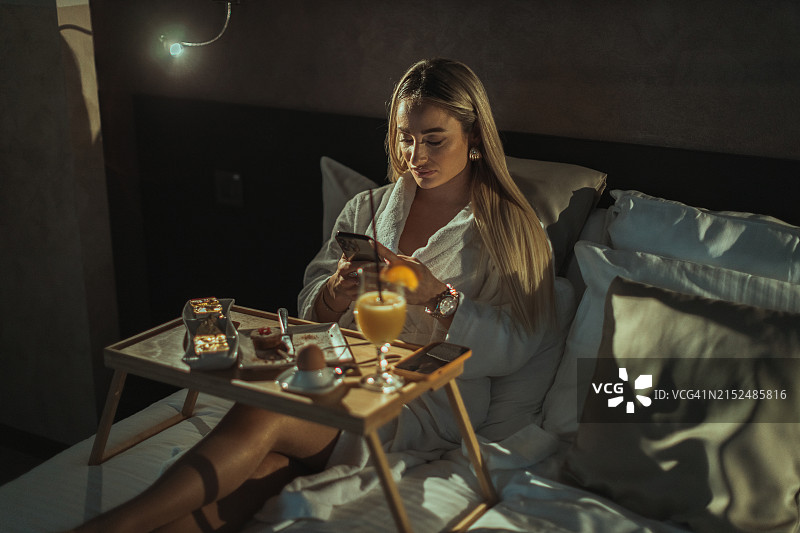 女子在酒店房间使用智能手机并享用客房服务图片素材