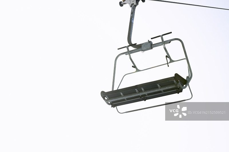 仰视空无一人的金属缆车，背景是晴朗天空下的山图片素材