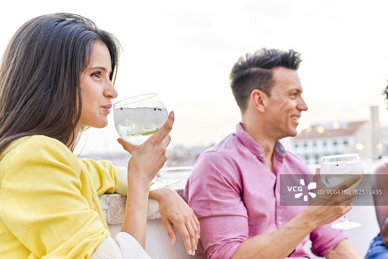 一群人坐在屋顶家具旁，围着桌子喝白葡萄酒图片素材