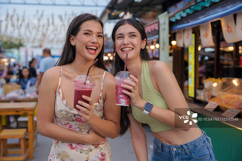年轻女子在街头小吃市场享用鲜榨果汁图片素材