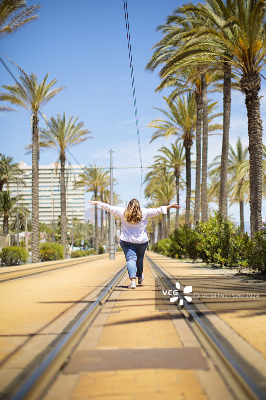年轻的数码游民女性，背着背包走在海滩城市，高兴地举起双臂图片素材
