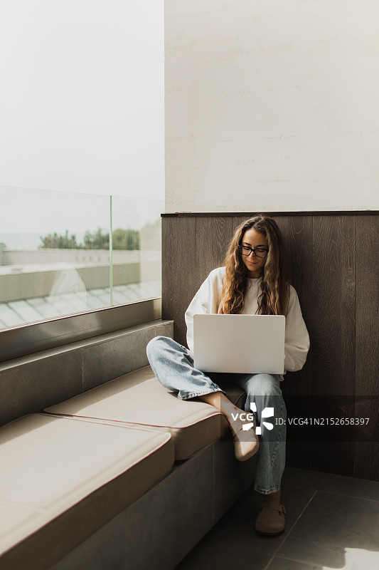 在酒店、咖啡馆或大学的室外露台上用笔记本电脑工作的自由职业者或女学生图片素材