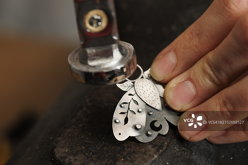 女珠宝商手工制作小盒吊坠，使用金属锤。珠宝工匠工作室图片素材