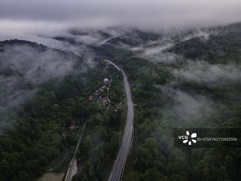 雾中绿色森林的空中山路之旅。图片素材