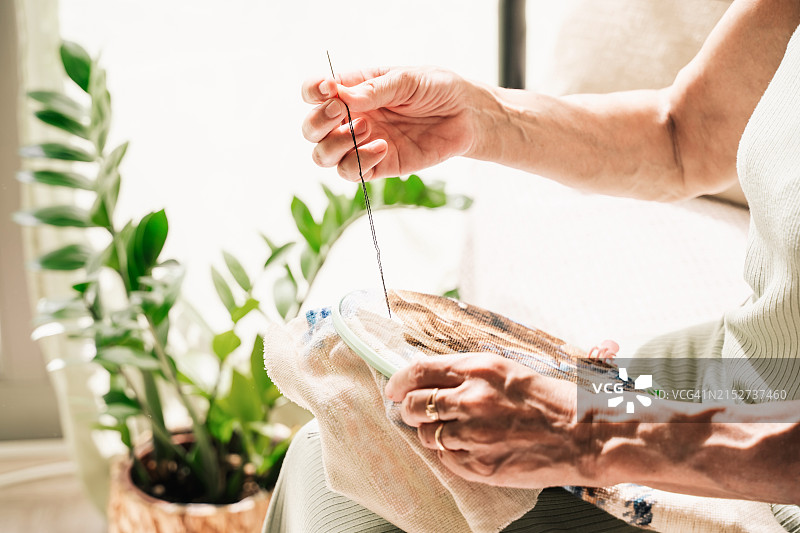 一位年长的妇女在阳光明媚的日子里在家刺绣，慢生活理念图片素材