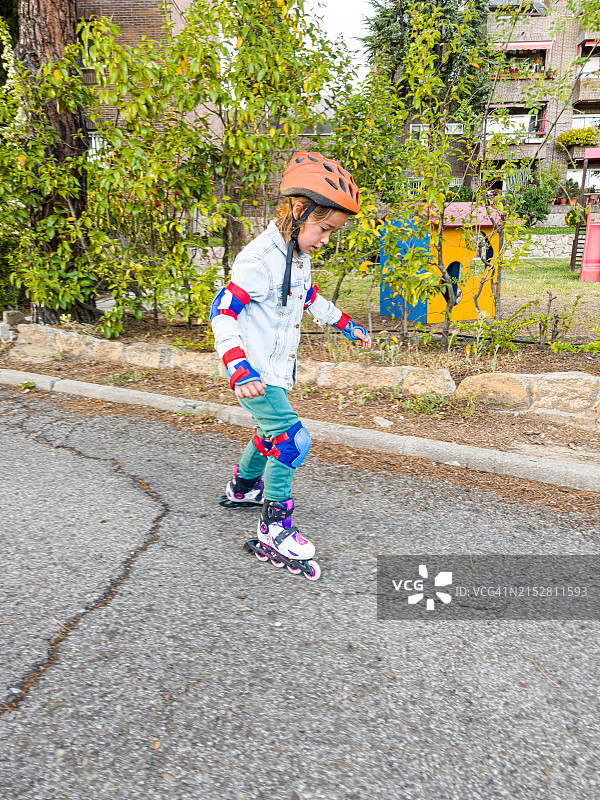 戴着护膝、护肘和护腕的女孩溜冰，学习滑冰，侧面视角。关于运动、学习、摔倒和站起来的概念图片素材