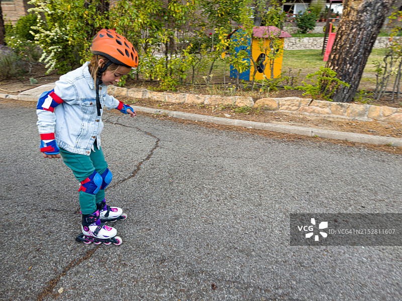 戴着护肘、护腕和护膝的女孩在溜冰，学习滑冰，侧身。 运动、学习、跌倒和站起来的概念。图片素材