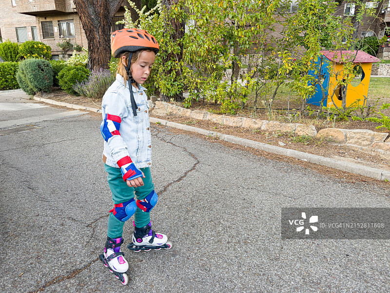 戴着护肘、护腕和护膝的女孩在溜冰，学习滑冰，侧身。 运动、学习、跌倒和站起来的概念。图片素材