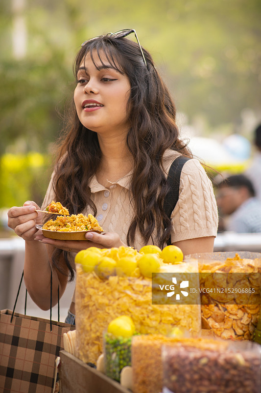 在街头市场吃印度街头小吃（印度米）的快乐年轻女人图片素材