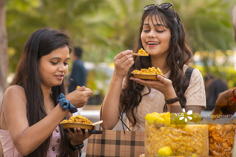 两位年轻女性朋友在街头市场吃印度街头小吃图片素材