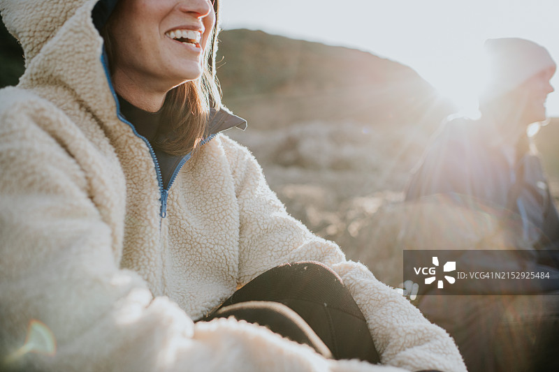 坐在海岸边的岩石上，和朋友们一起微笑的女人特写图片素材