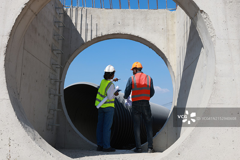 两位建筑工程师在建筑工地讨论蓝图房屋建造计划，矩形混凝土排水系统基础设施图片素材