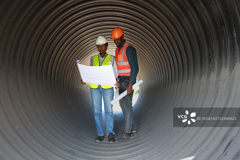 两位建筑工程师正在大型管道或隧道中工作，他们手持蓝图图片素材