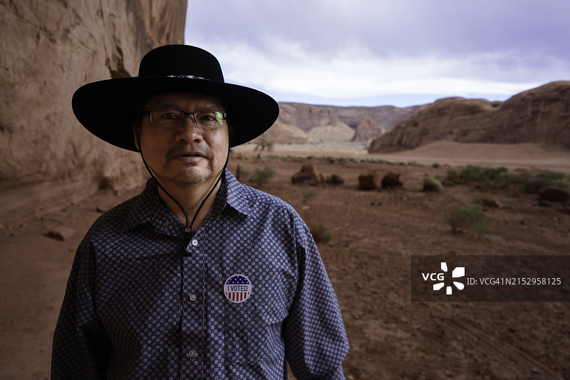 在犹他州纪念碑谷部落公园图腾柱岩前，一位四十多岁的纳瓦霍族男人拿着一张“我已投票”贴纸，表明她刚刚在美国大选中投票图片素材