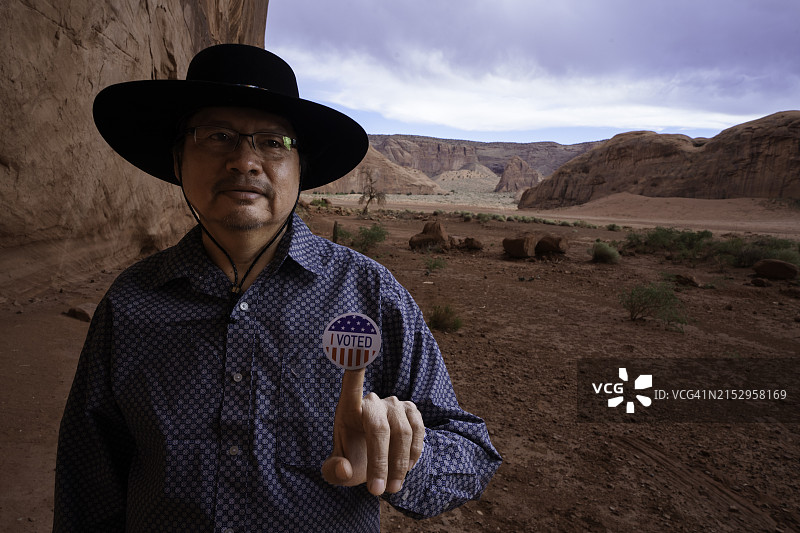 在犹他州纪念碑谷部落公园图腾柱岩前，一位四十多岁的纳瓦霍族男人拿着一张“我已投票”贴纸，表明她刚刚在美国大选中投票图片素材