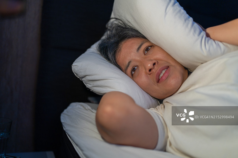被噩梦困扰，用枕头捂住耳朵的女人图片素材