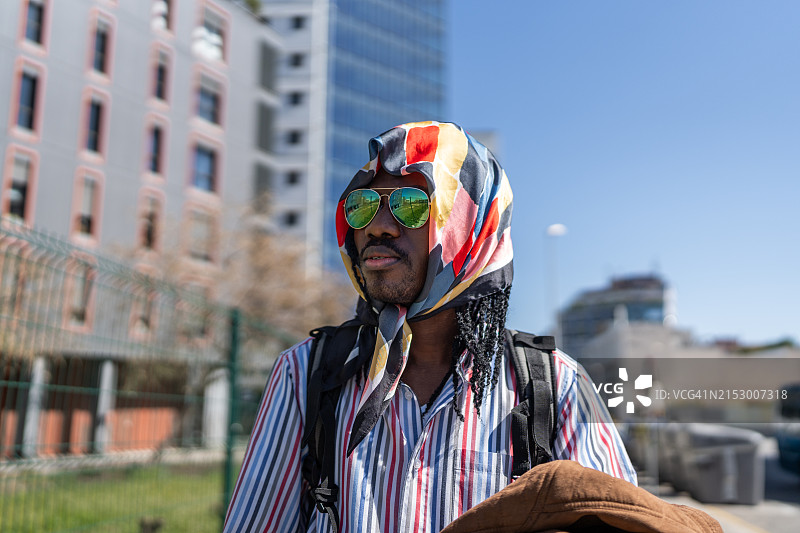 戴着彩色围巾和太阳镜的男人站在建筑物前图片素材