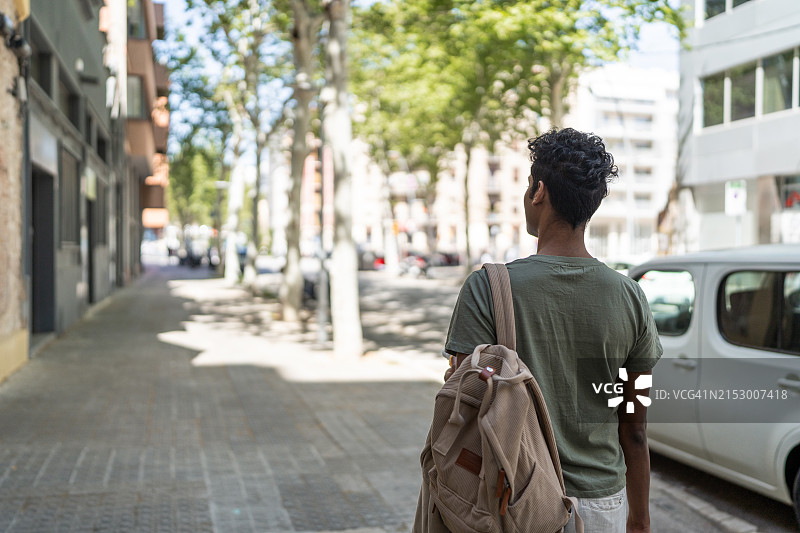 男子身穿绿色衬衫，背着背包走在街上图片素材