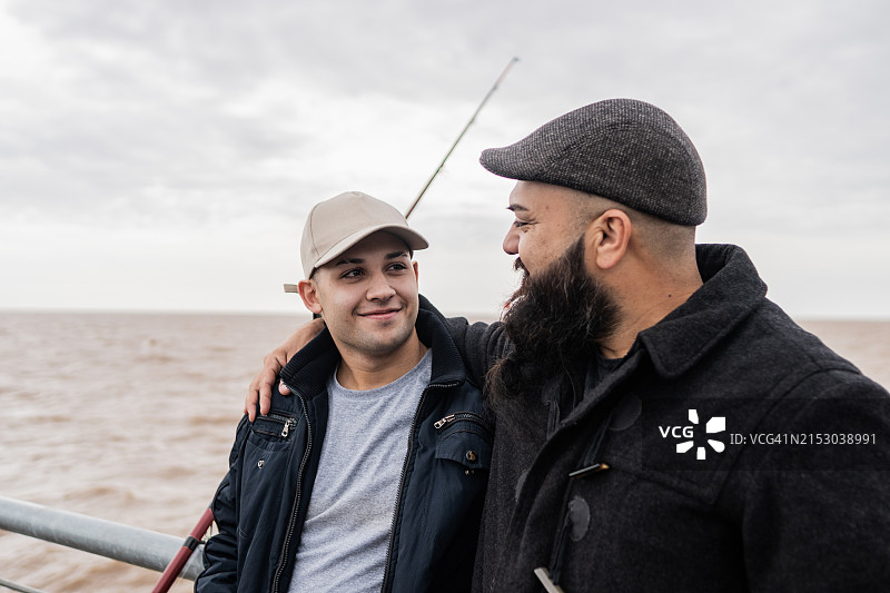 父子在阿根廷拉普拉塔河钓鱼时拥抱交谈图片素材