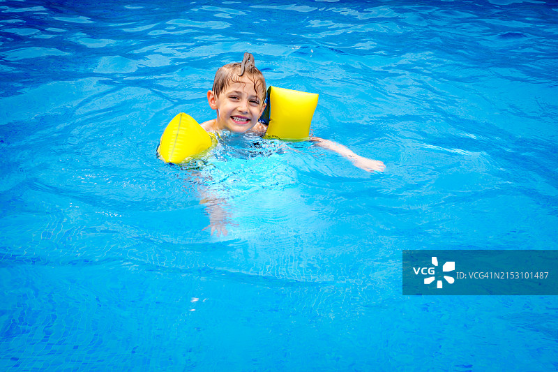 在游泳池里戴着袖标、对着镜头露出牙齿微笑的小男孩肖像图片素材