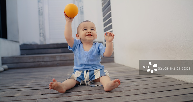 宝宝快乐地在家里地板上玩小球，促进儿童发育、运动技能和成长。幼儿在家里的地上笑着学习玩具，进行游戏、日托和有趣的创造图片素材