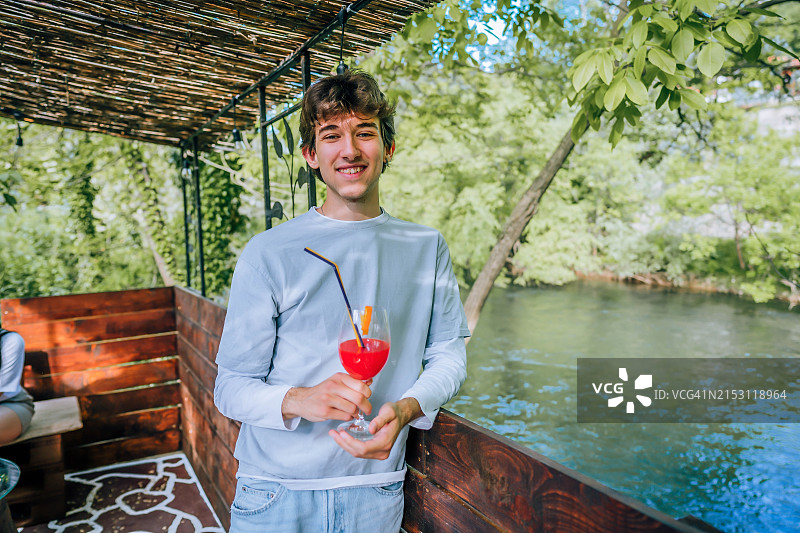 在河边享受大自然的男人，手里拿着鸡尾酒图片素材