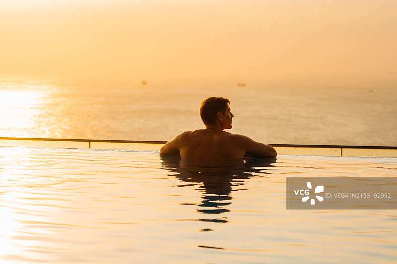 男人在日落时分的无边泳池放松，欣赏壮丽的海景图片素材