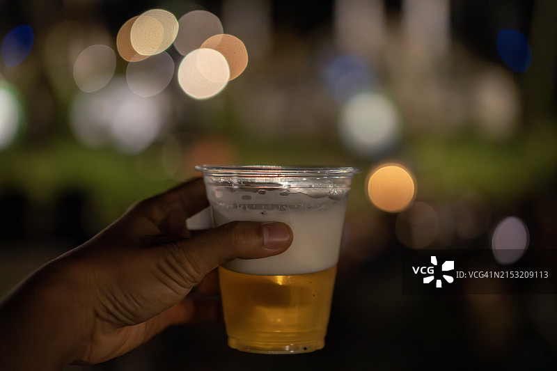 手持啤酒杯，散景灯光背景图片素材