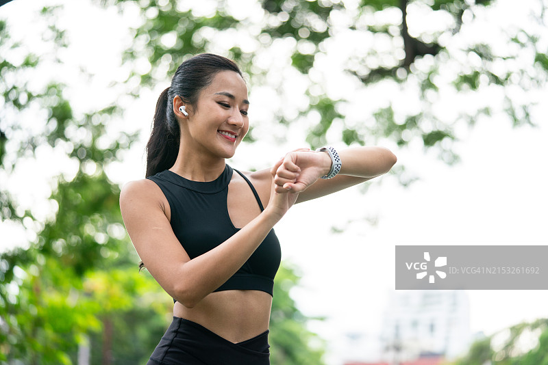 年轻亚洲女跑步者休息时查看智能手表图片素材