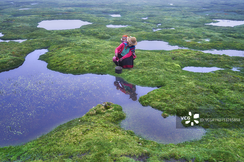 秘鲁安第斯山脉：克丘亚-奎罗族妇女背着婴儿在池塘里取水图片素材