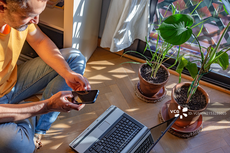 成熟男人坐在家中木地板上使用手机的俯视图图片素材