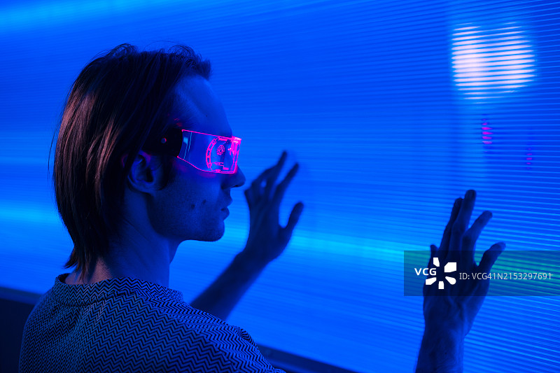 戴智能霓虹眼镜的未来主义男人触摸霓虹墙背景图片素材