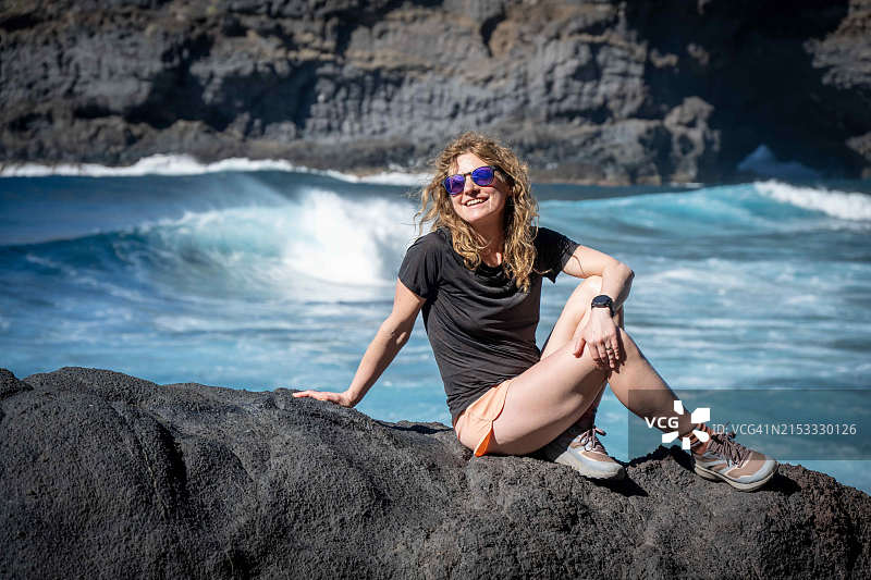 年轻女人坐在西班牙拉帕尔马岛北部布哈伦海滩的一块大石头上图片素材
