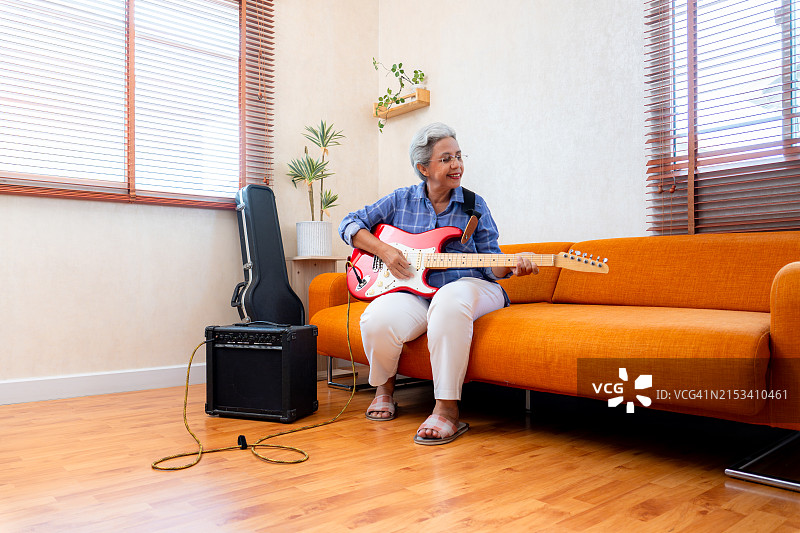快乐的亚洲退休老年妇女在家玩电吉他图片素材