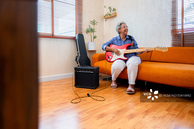 快乐的亚洲退休老年妇女在家玩电吉他图片素材