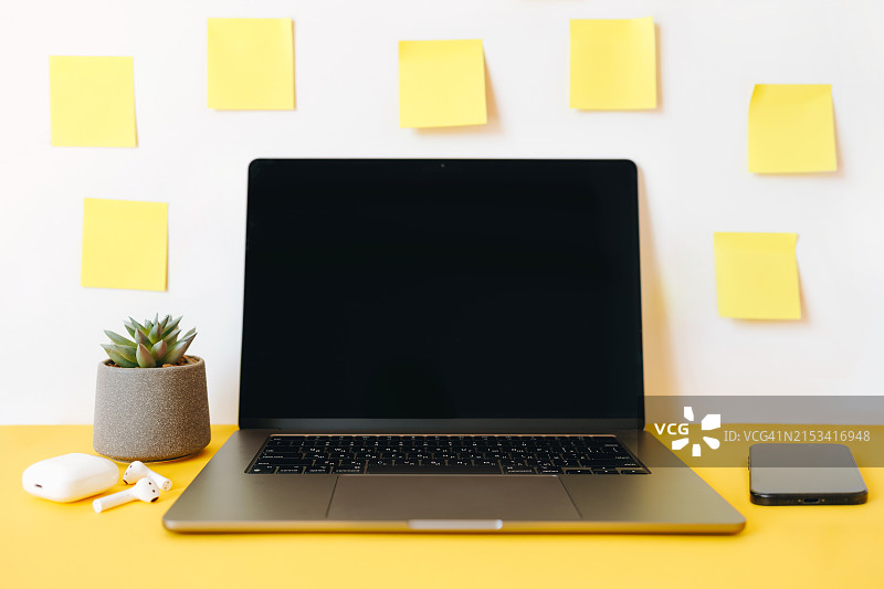 舒适的工作空间：带有笔记本电脑、黄色便签纸和办公用品小工具，家庭办公室、多任务处理、自由职业概念图片素材